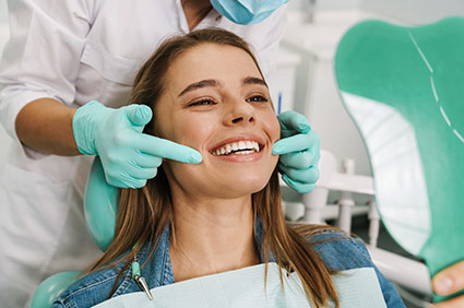 Female patient smiling and looking in a mirror as dentist points to teeth